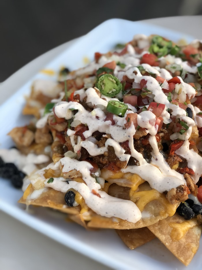 Sheet pan loaded with melted cheese beef nachos, jalapeΓ±os, and sour cream