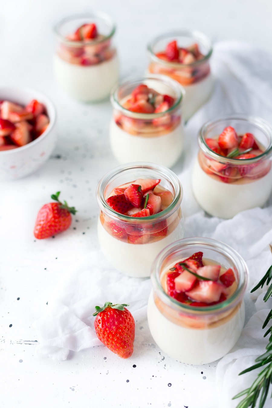 Glass ramekins of chilled silky yellow lemon posset garnished with lemon zest and raspberries