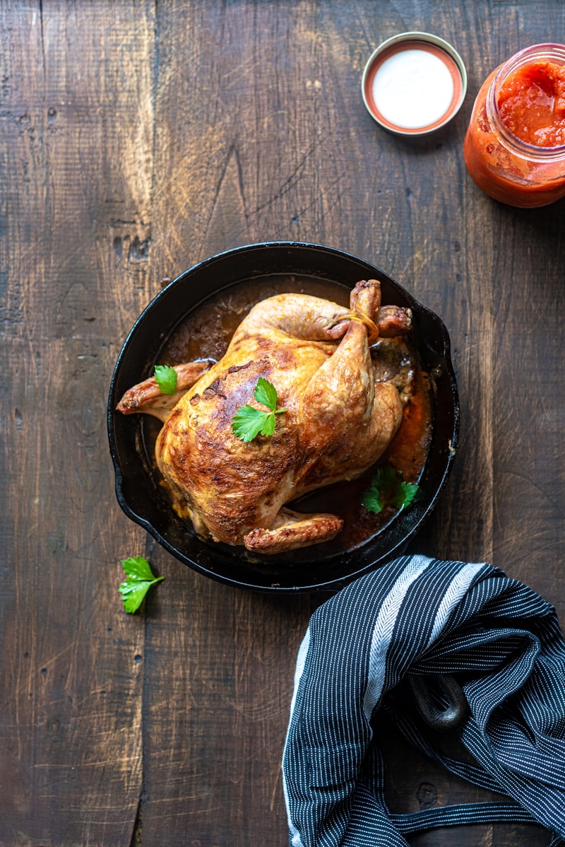 Golden-brown crisp roast chicken surrounded by caramelized onions and carrots on rustic carving board